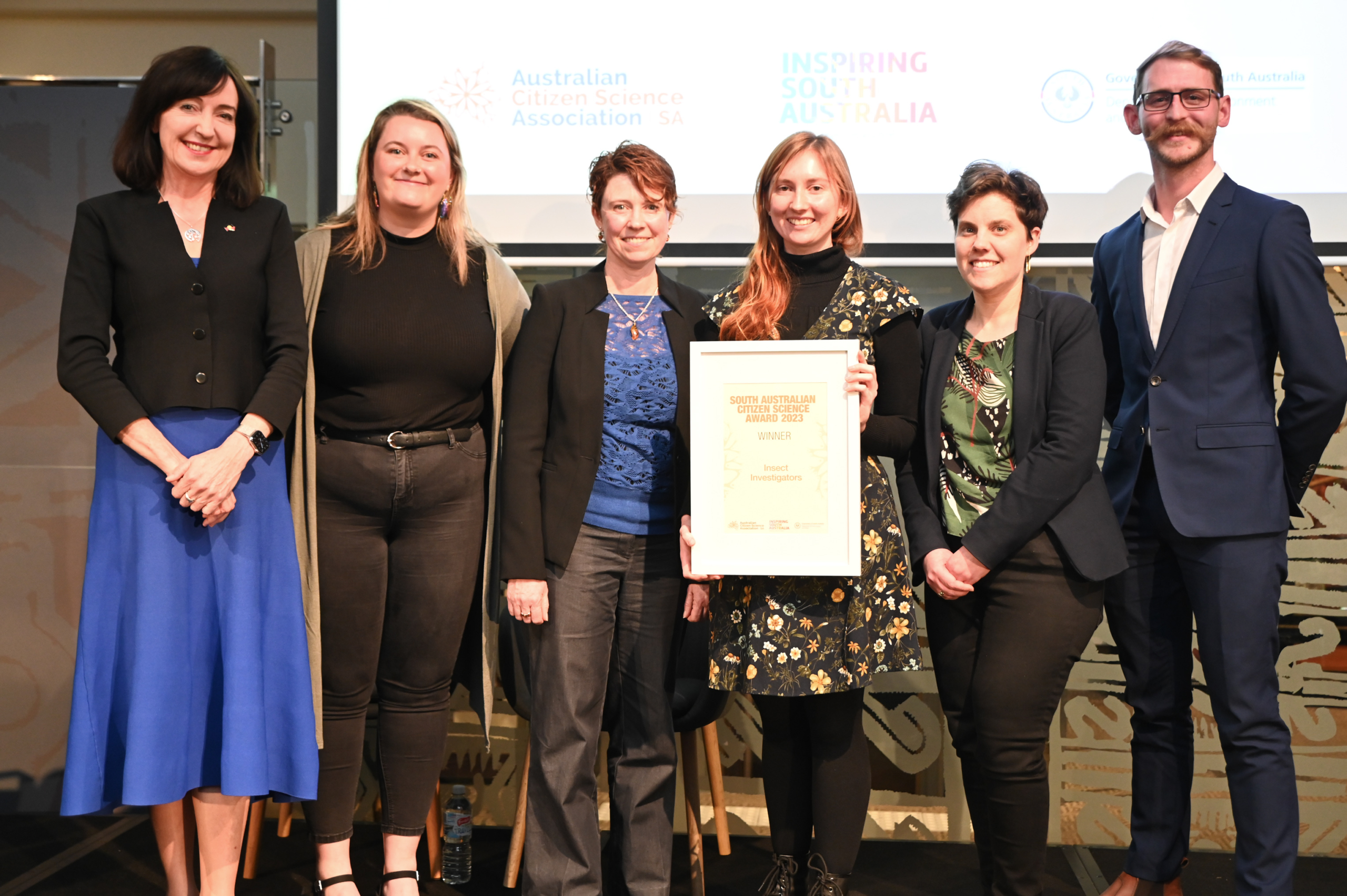 6 people stand on a stay with the 4th person from the left holding the Citizen Science Award winner certificate.